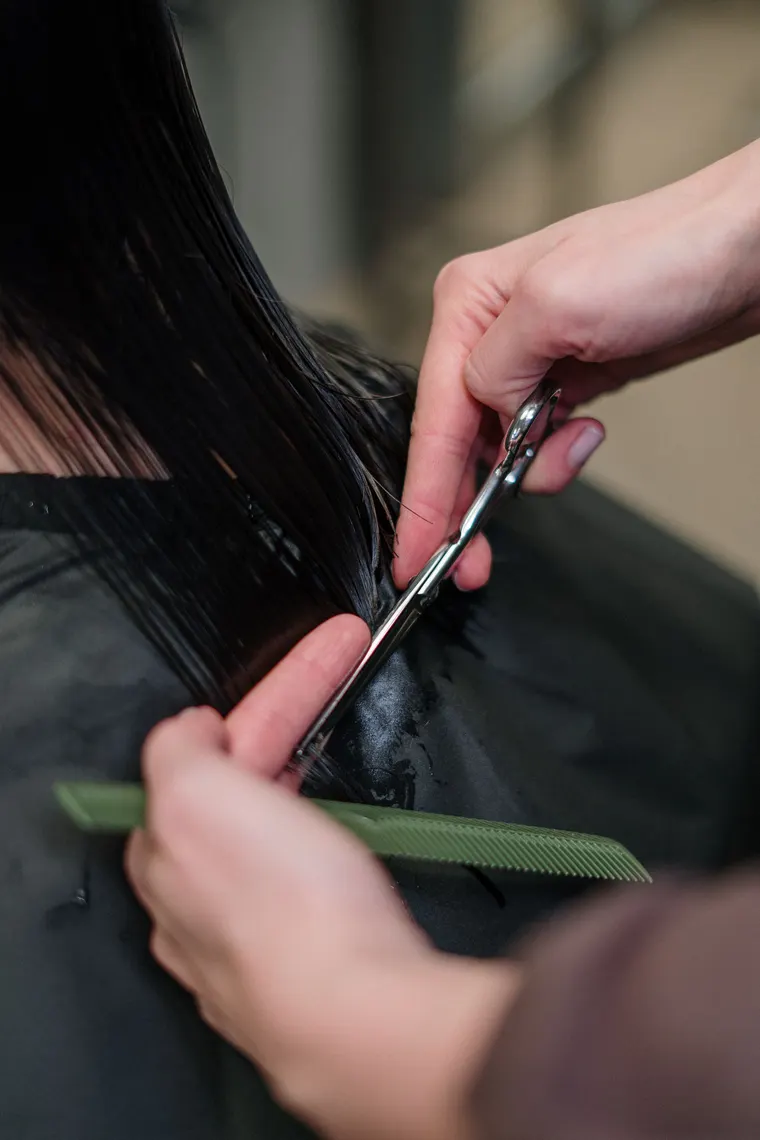 Coiffeuse schneidet langes, dunkles Haar mit Schere und Kamm